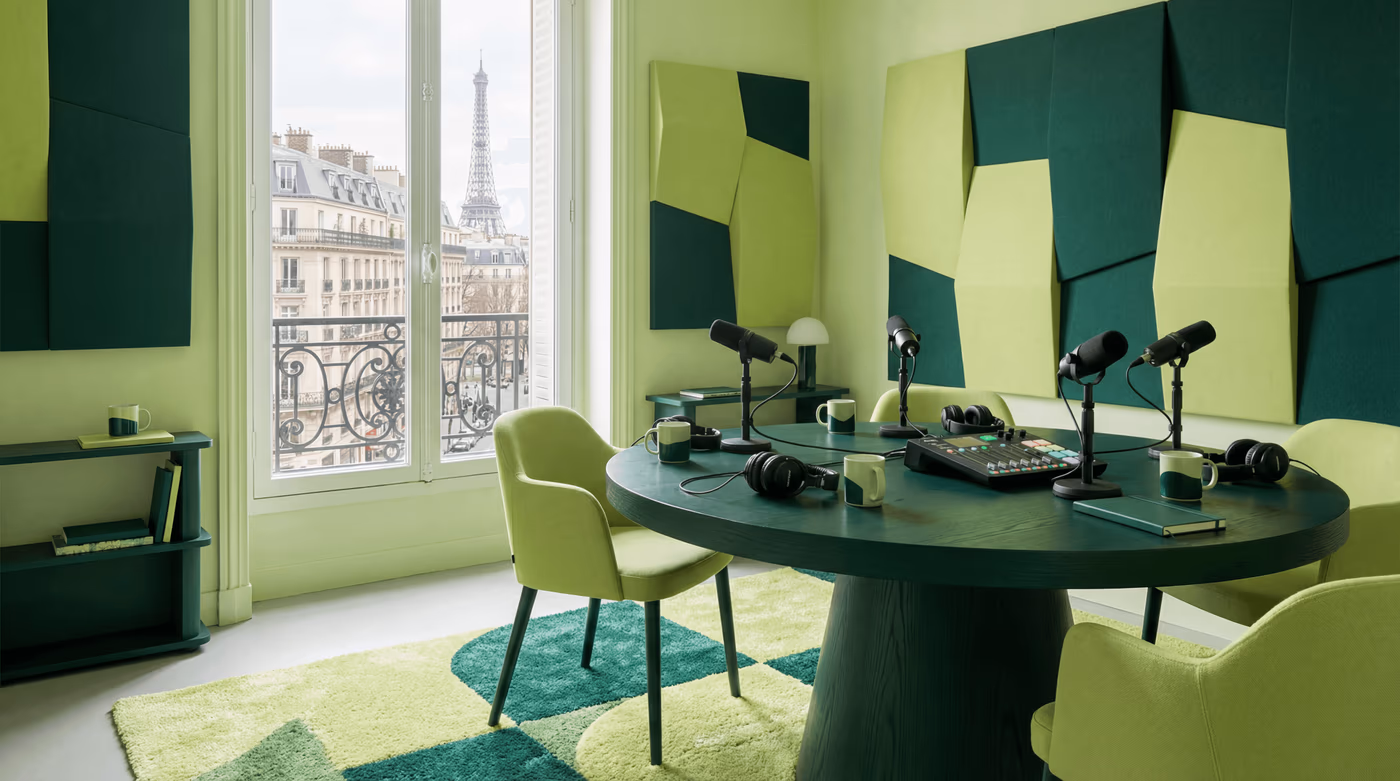 Studio de podcast avec table ronde, quatre micros, console et panneaux acoustiques verts, vue sur la tour Eiffel
