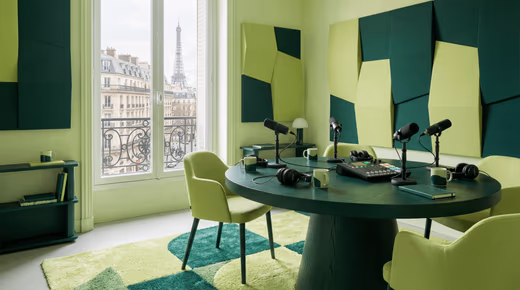 Studio de podcast avec table ronde, quatre micros, console et panneaux acoustiques verts, vue sur la tour Eiffel