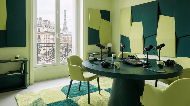 Studio de podcast avec table ronde, quatre micros, console et panneaux acoustiques verts, vue sur la tour Eiffel